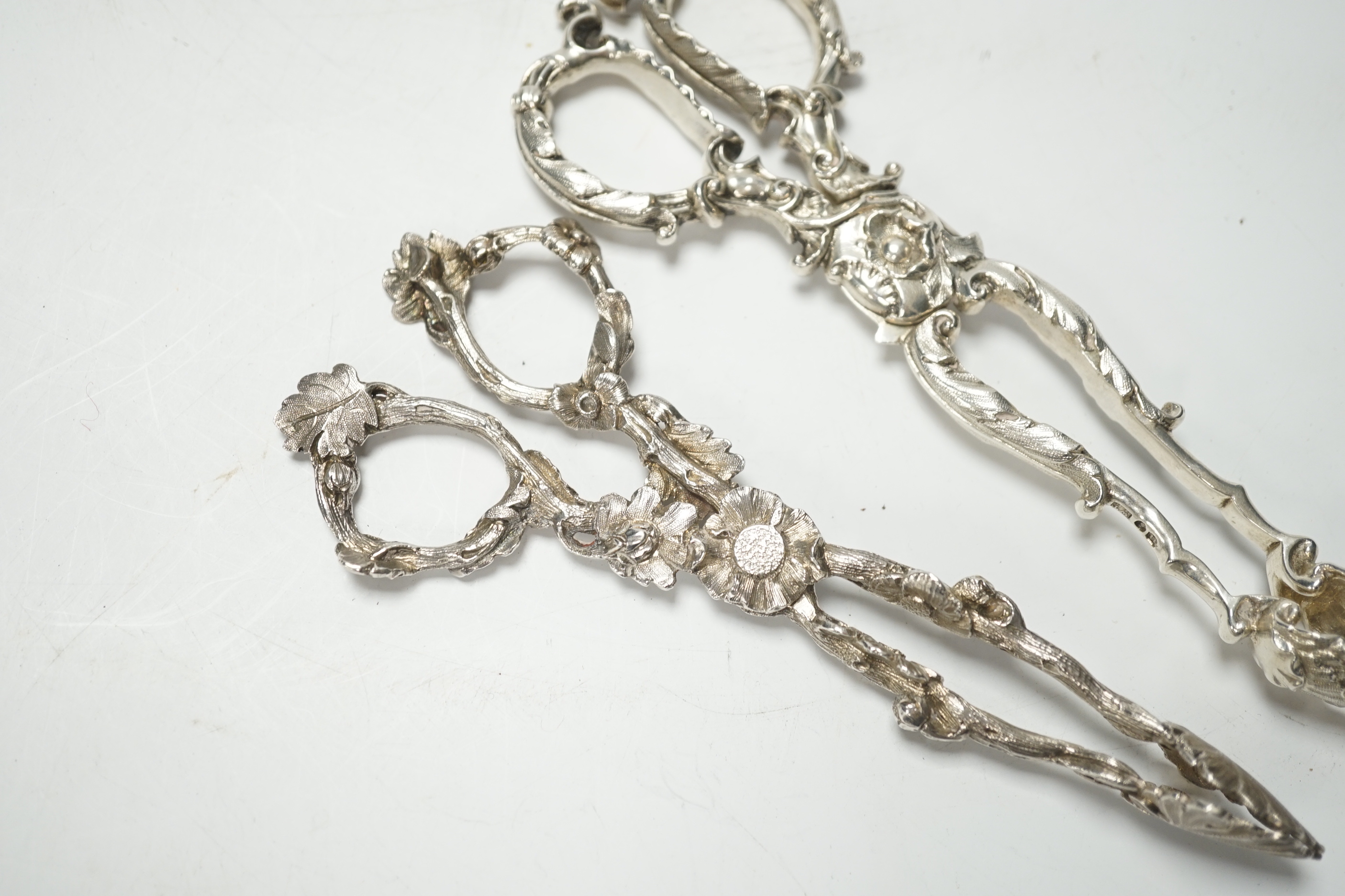 A pair of Victorian cast silver sugar tongs, of foliate design, by George Adams, London, 1871, 14.2cm and a pair of William IV cast silver sugar tongs, by Theobalds & Bunn, London, 1835, 15.4cm, 102 grams.